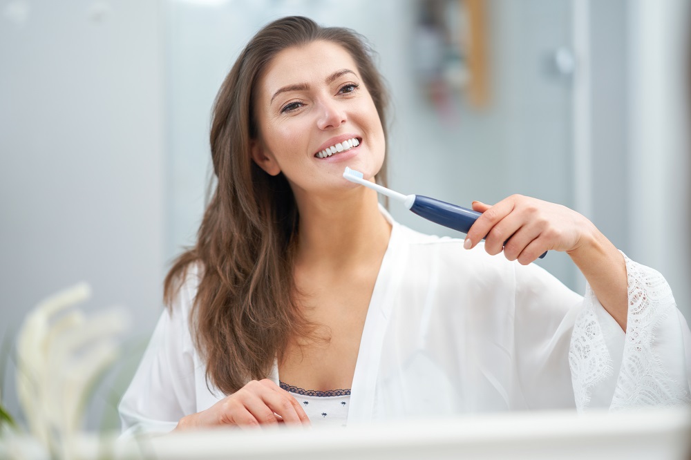 kobieta myje zęby szczoteczką soniczną